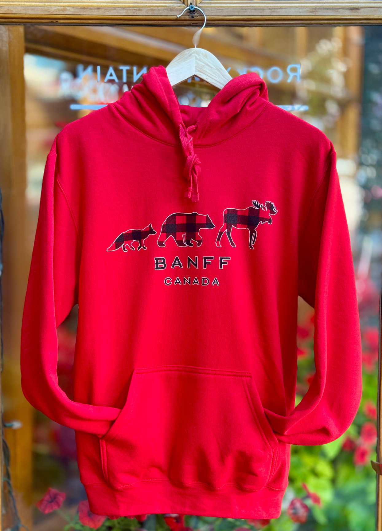 Red hoodie with bear, buffalo, and moose design and 'Banff Canada' text on a hanger.