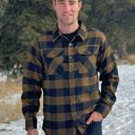 A man wearing a black and brown buffalo check flannel shirt with two flap breast pockets and two button cuff, standing with one hand in his front pocket.