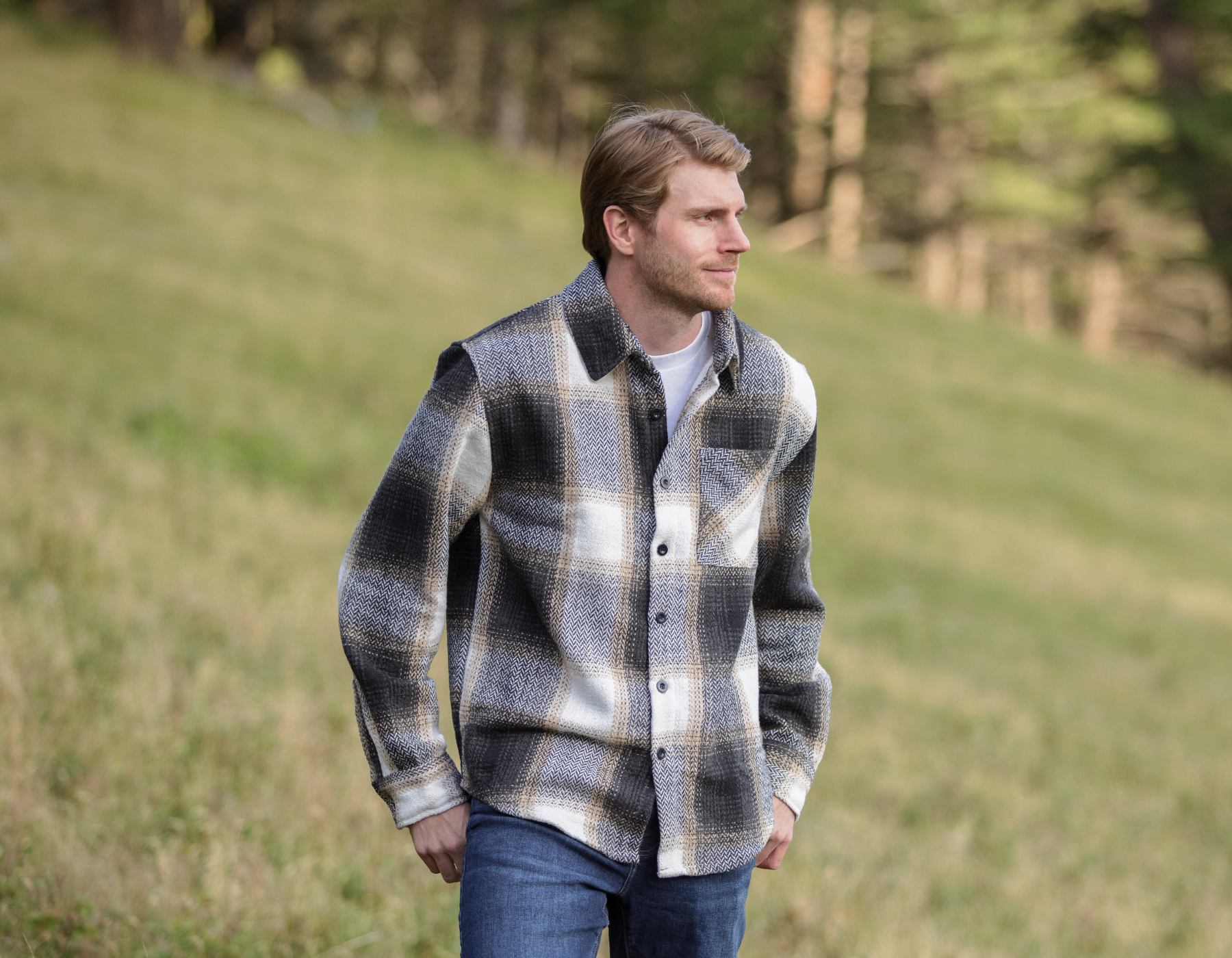 A person standing in an open field wearing a plaid flannel jacket with a herringbone weave, button-up collar, and long sleeves.