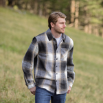 A person standing in an open field wearing a plaid flannel jacket with a herringbone weave, button-up collar, and long sleeves.