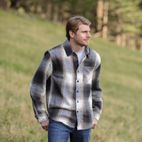 A person standing in an open field wearing a plaid flannel jacket with a herringbone weave, button-up collar, and long sleeves.