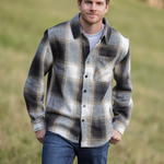 A person standing in an open field wearing a plaid flannel shacket with a herringbone weave, button-up collar, and long sleeves.