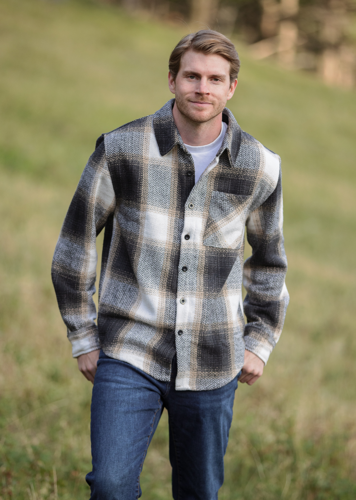 A person standing in an open field wearing a plaid flannel shacket with a herringbone weave, button-up collar, and long sleeves.