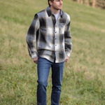 A person standing in an open field wearing a plaid flannel jacket with a herringbone weave, button-up collar, and long sleeves.