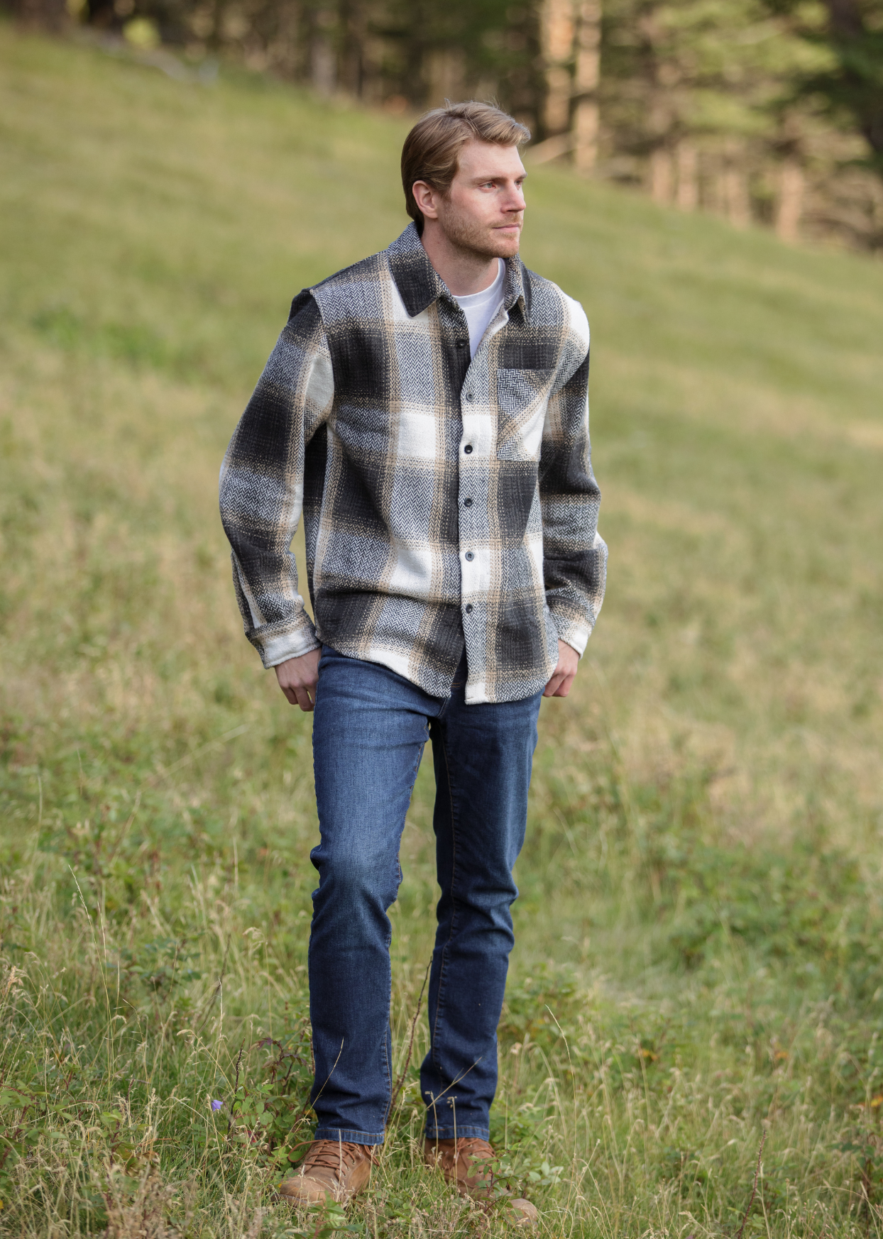 A person standing in an open field wearing a plaid flannel jacket with a herringbone weave, button-up collar, and long sleeves.