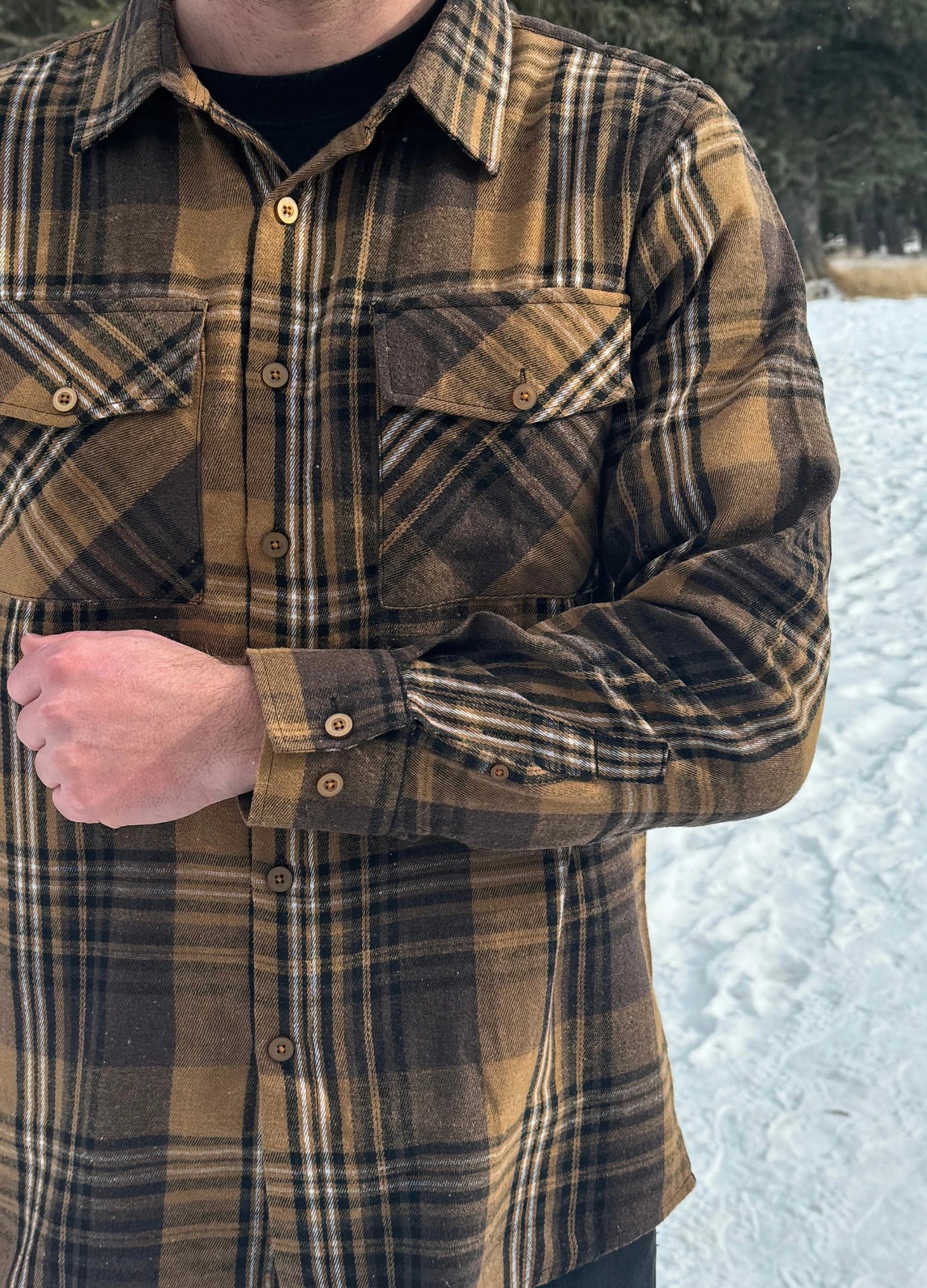 A man wearing a mocha brown flannel shirt with two flap breast pockets and a shirt tail hemline, standing outdoors.