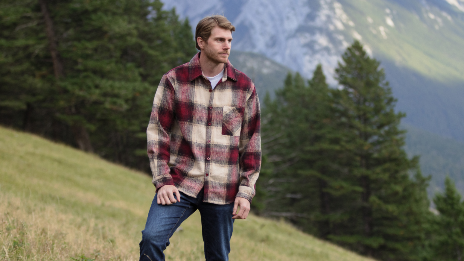 Man standing in a field, with mountains in the background.