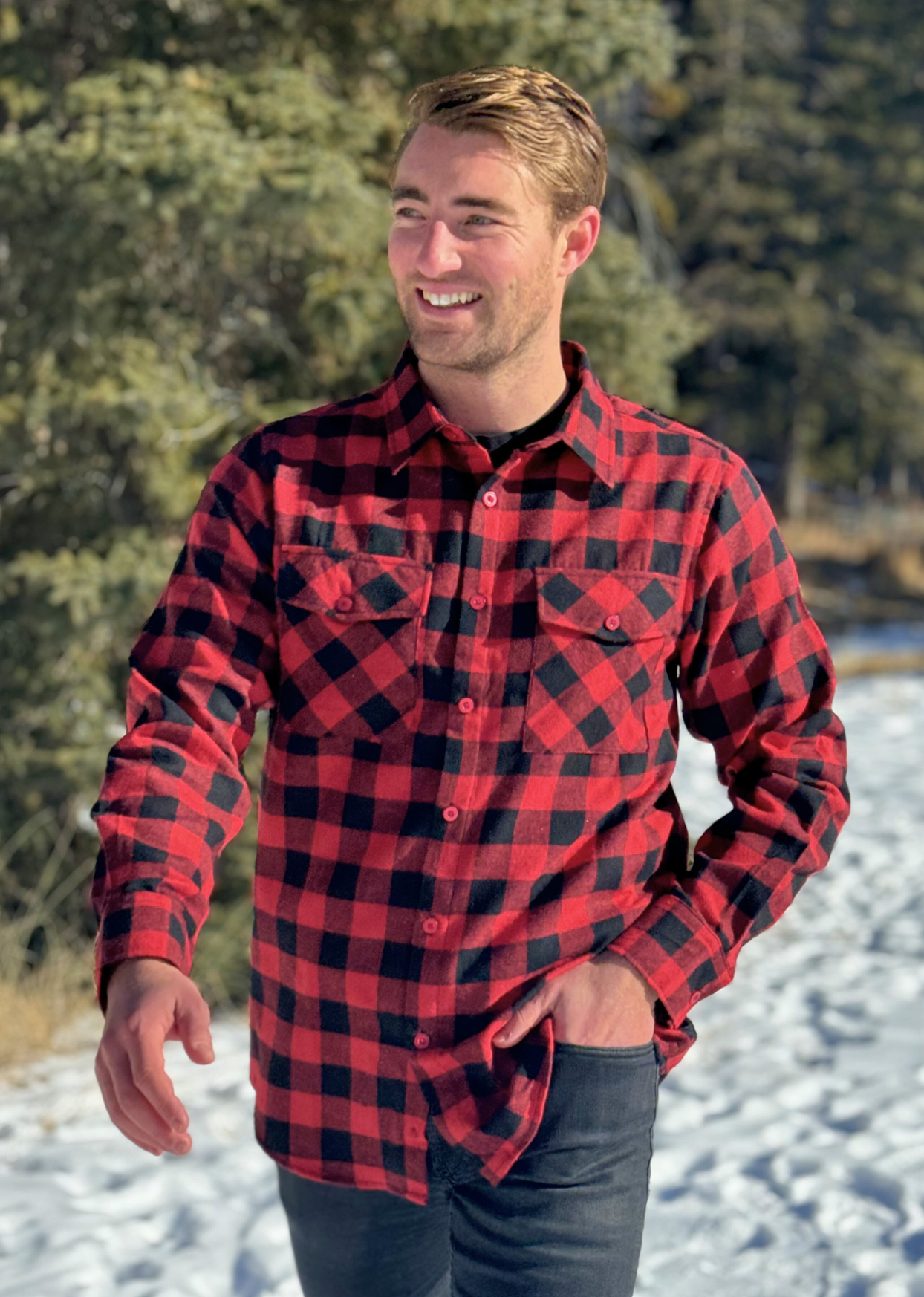 A man wearing a red and black buffalo check flannel shirt with two flap breast pockets and a button cuff, standing outdoors. This is an action shot, he is walking.