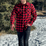 A man wearing a red and black buffalo check flannel shirt with two flap breast pockets and a button cuff, standing outdoors.