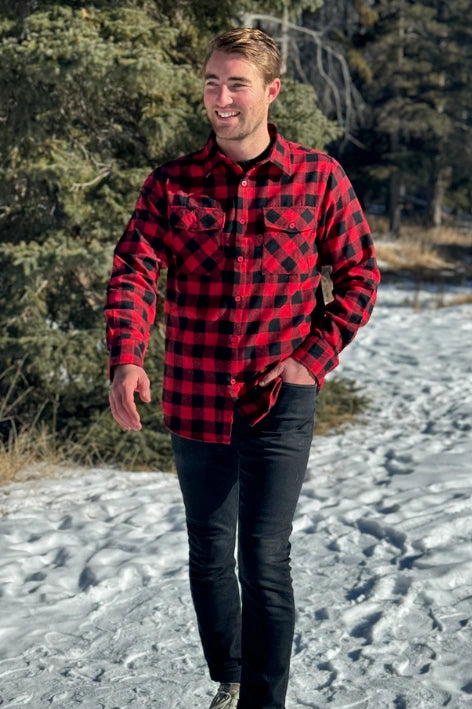 A man wearing a red and black buffalo check flannel shirt with two flap breast pockets and a button cuff, standing outdoors.
