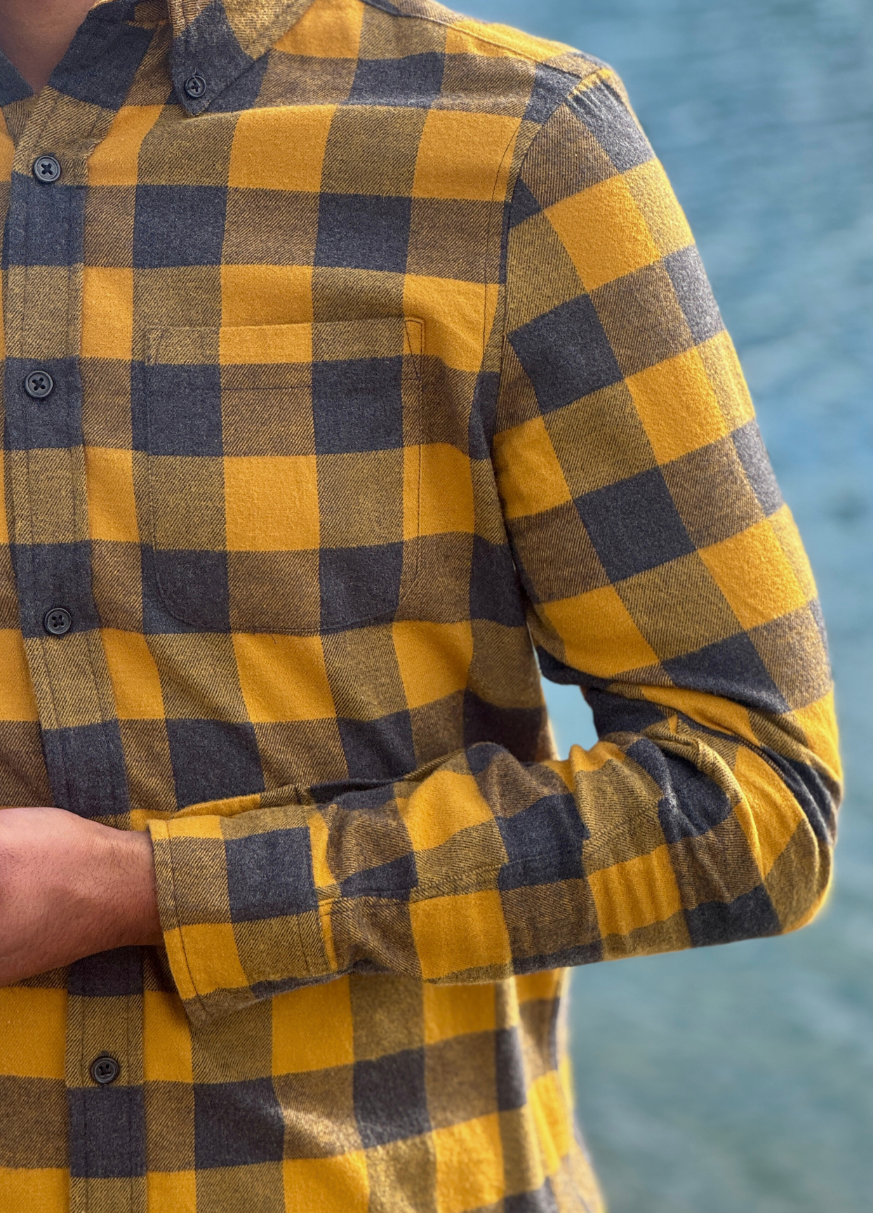 Gold and grey checkered shirt worn by a person with a blurred natural background