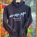 Black hoodie with white graphics and text 'Banff Canada' on a hanger in front of a glass door.