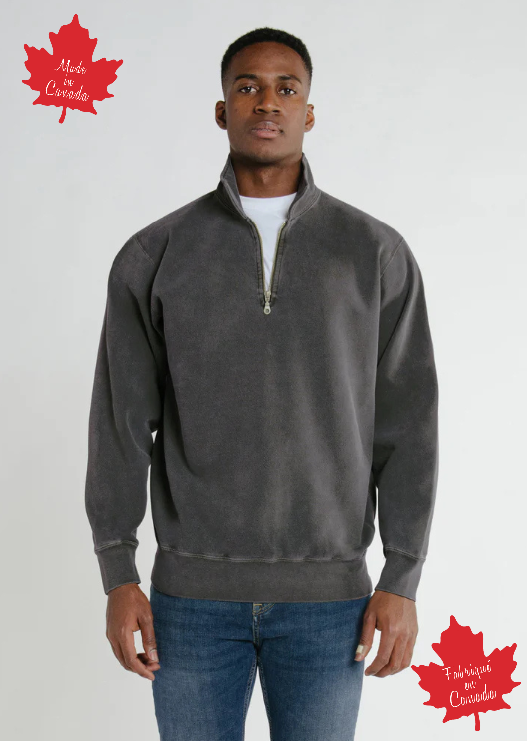 A person wearing a grey zip polo sweatshirt, standing against a plain background with a small red maple leaf logo in the corner, indicating that the garment was made in Canada.