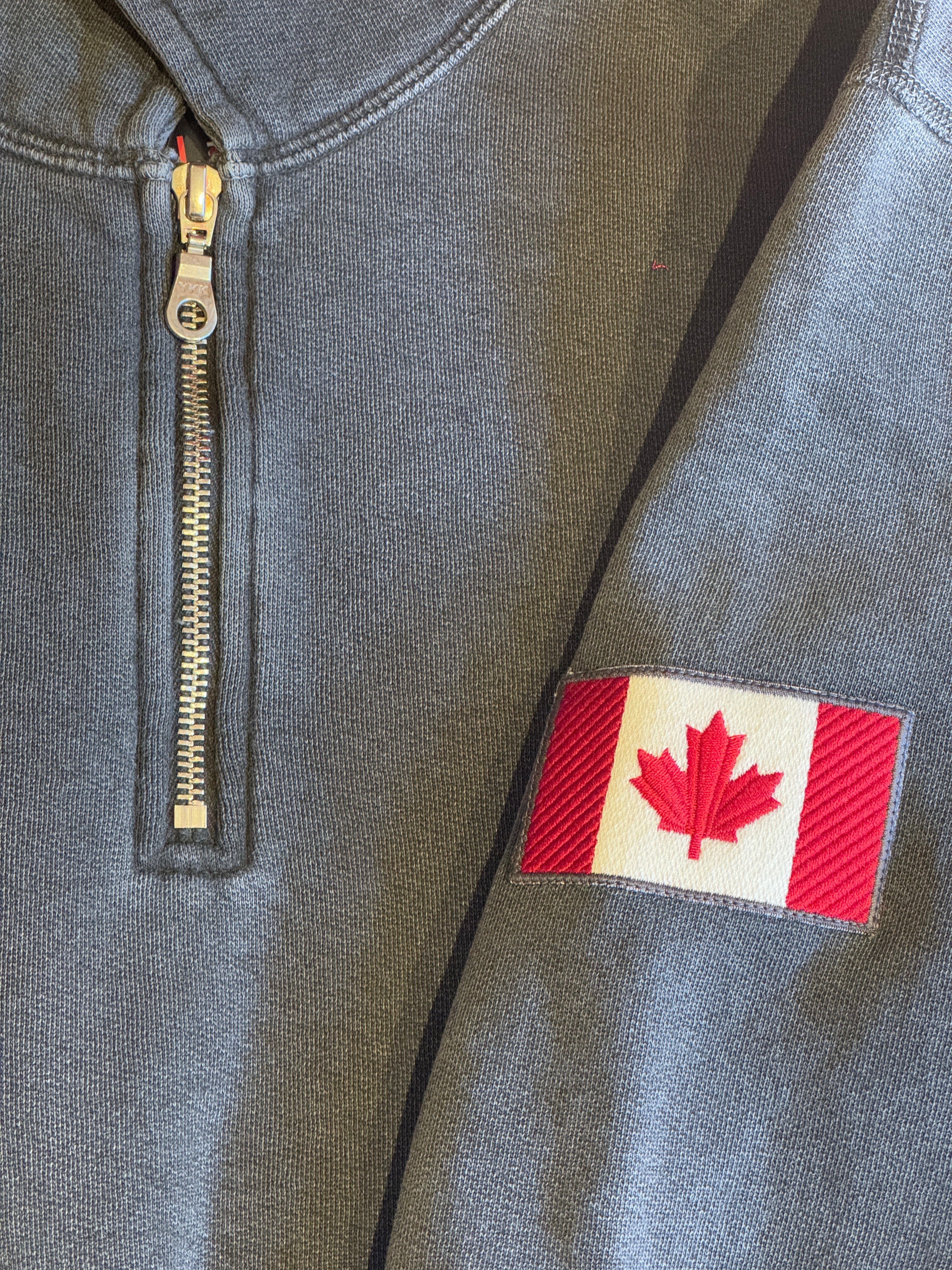 Gray jacket with a zipper and a red and white patch featuring a maple leaf.