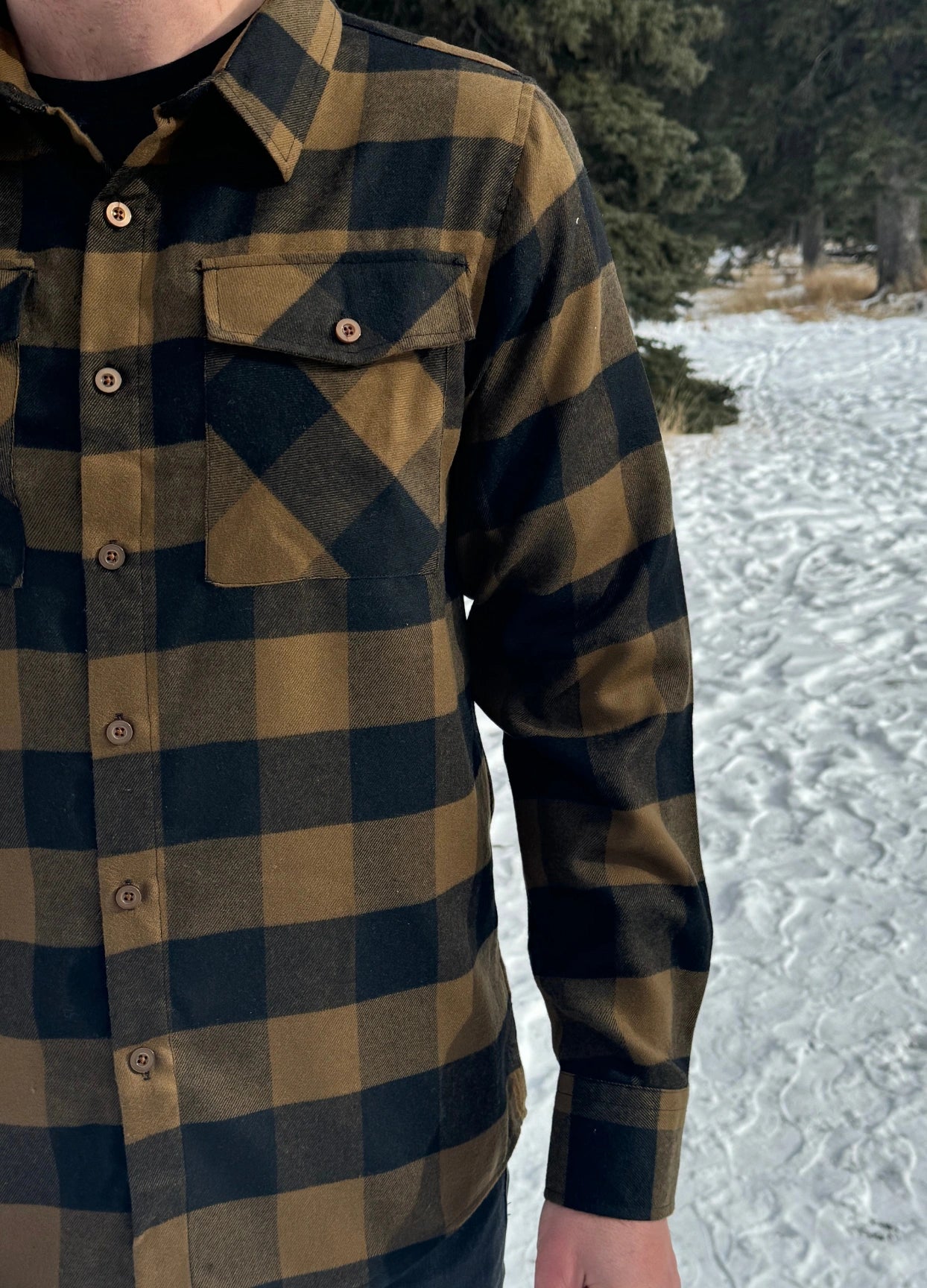 A man wearing a black and brown buffalo check flannel shirt with two flap breast pockets and two button cuff