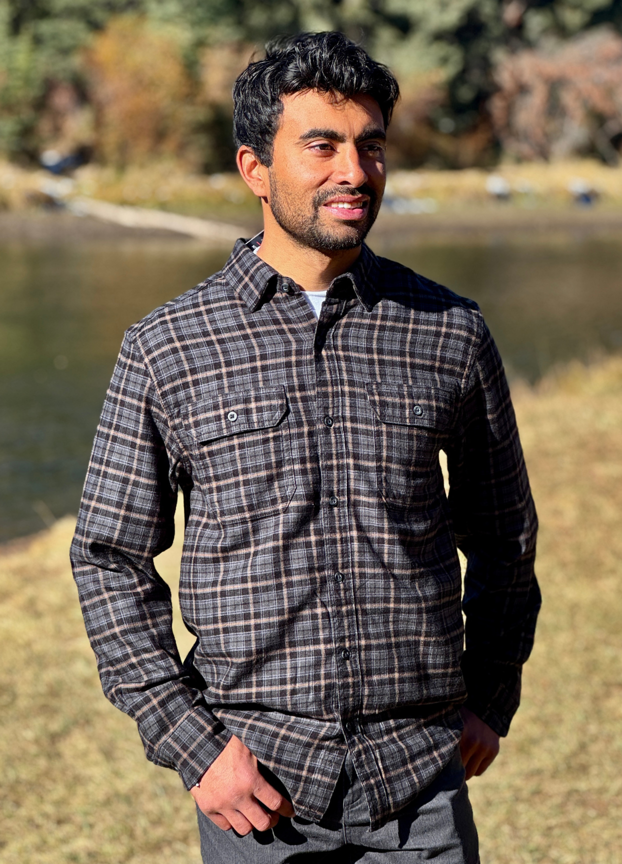 Man wearing a plaid flannel shirt standing outdoors by a river in Banff