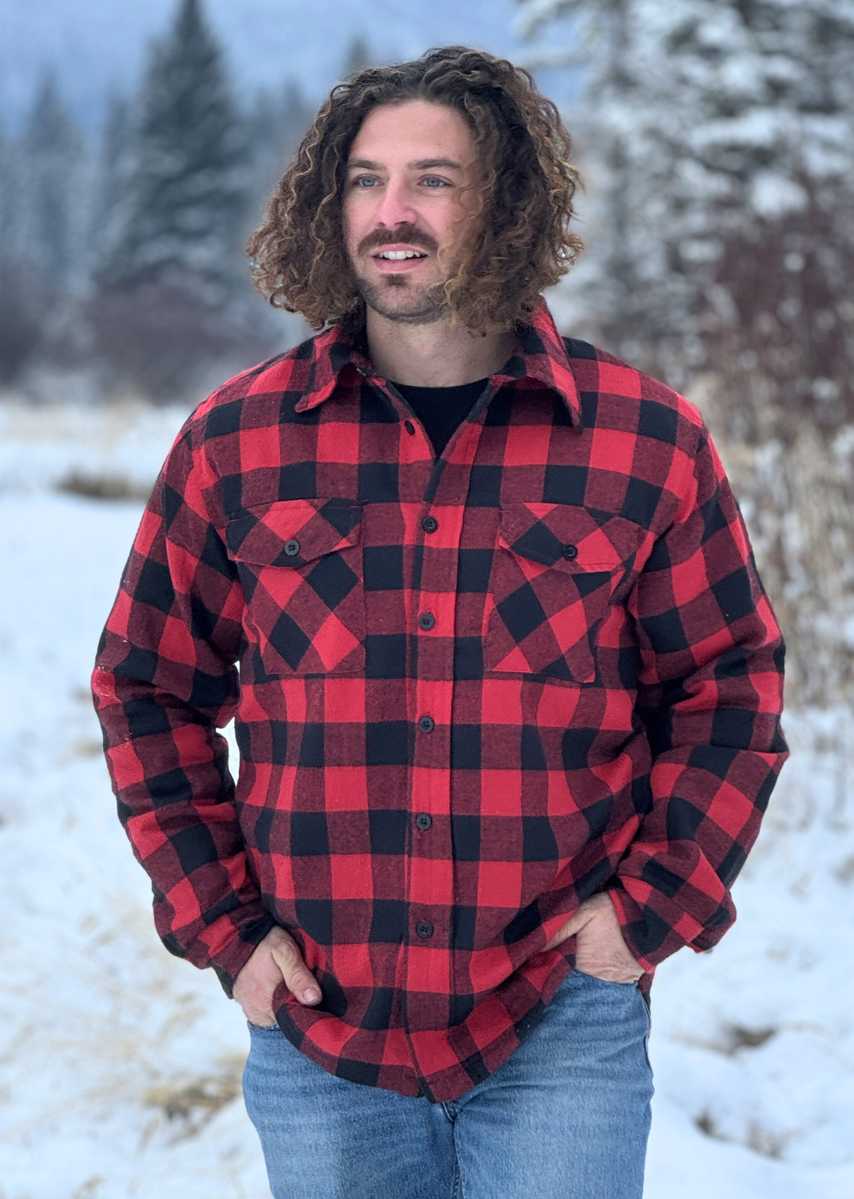 A man wearing a red and black checkered padded flannel jacket, standing outdoors in a snowy environment.