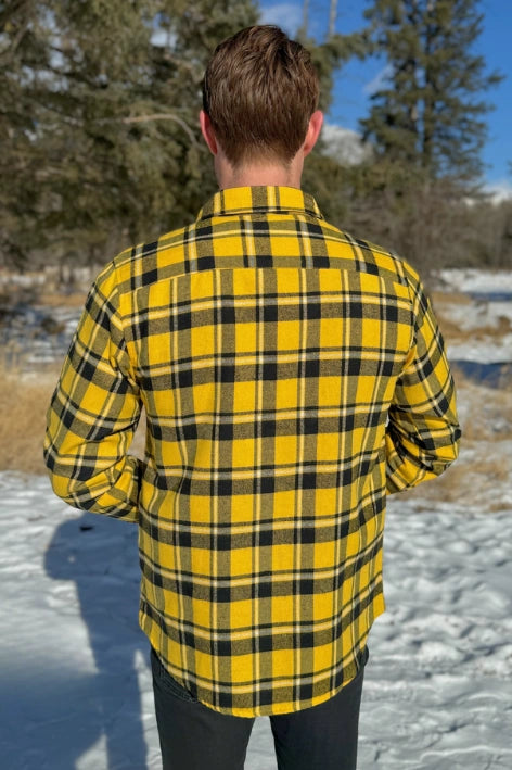 Back view of a man wearing a long-sleeved yellow and black flannel plaid shirt with two flap breast pockets and a button cuff.