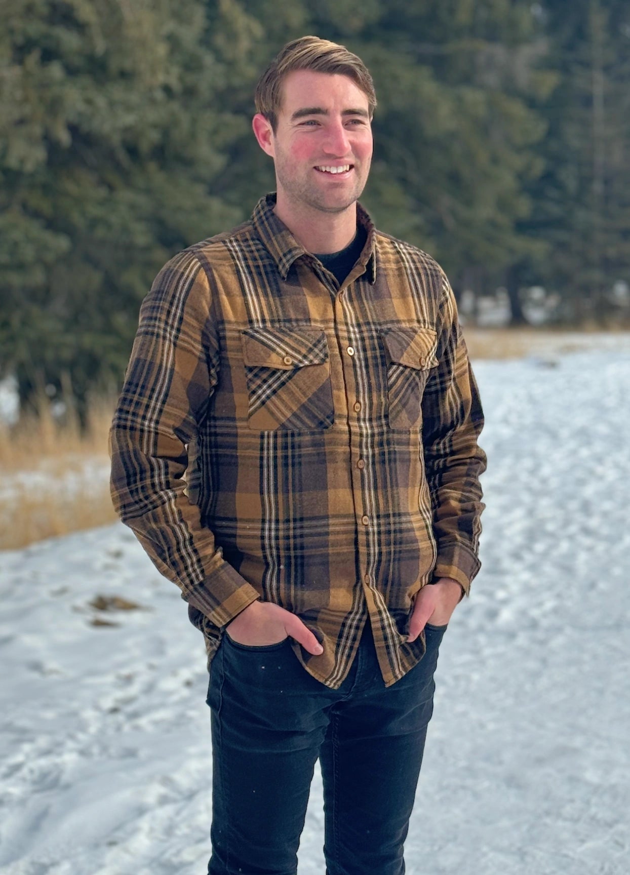 A man wearing a mocha brown flannel shirt with two flap breast pockets and a shirt tail hemline, standing outdoors.