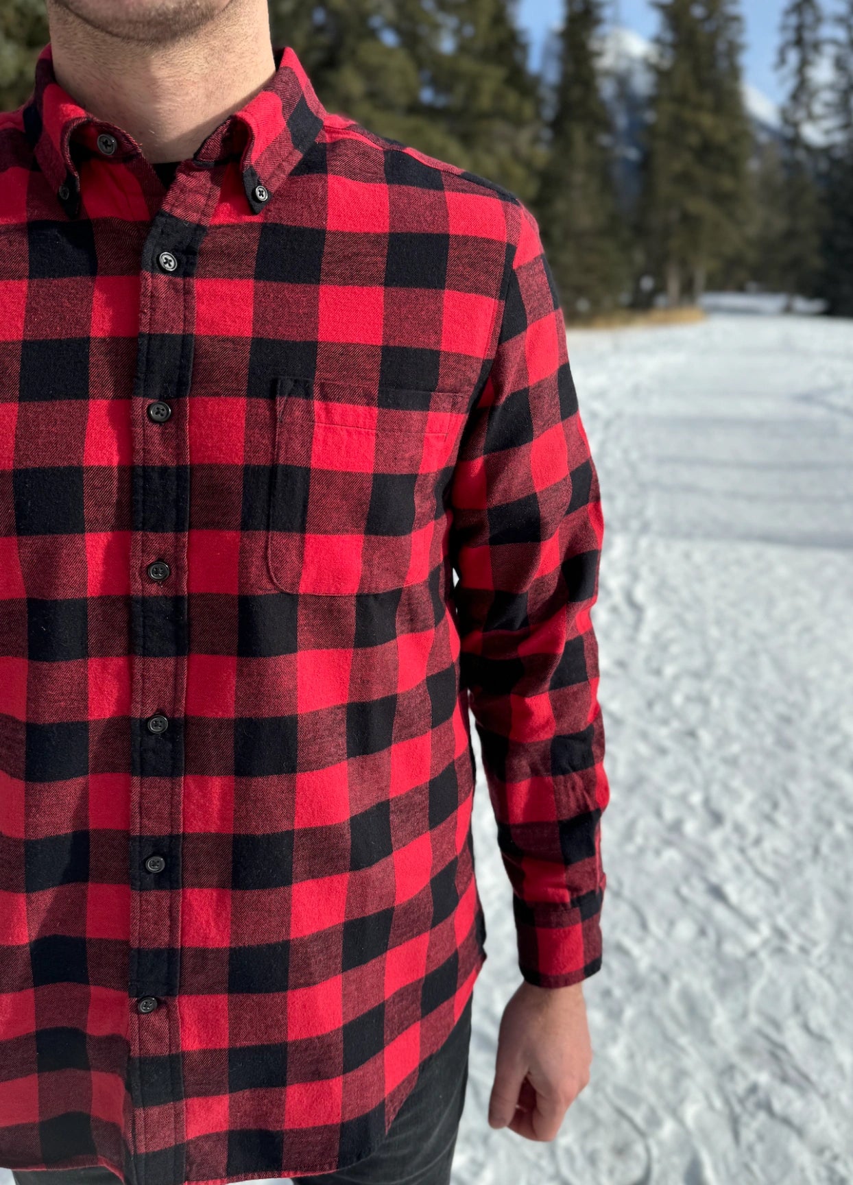 Close up of man wearing a classic Canadian red and black buffalo check button-down shirt with a single pocket on the chest.