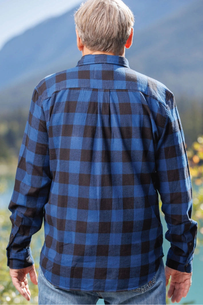 Back view of a man wearing a long-sleeved marine blue and black buffalo check flannel shirt and blue jeans, standing outdoors.