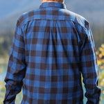 Back view of a man wearing a long-sleeved marine blue and black buffalo check flannel shirt and blue jeans, standing outdoors.