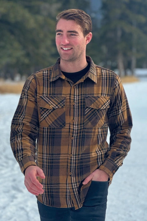 A man wearing a mocha brown flannel shirt with two flap breast pockets and a shirt tail hemline, standing outdoors.
