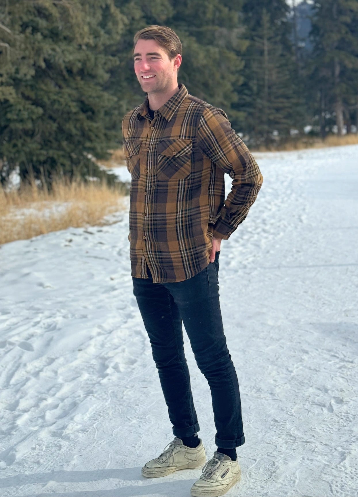 A man wearing a mocha brown flannel shirt with two flap breast pockets and a shirt tail hemline, standing outdoors.