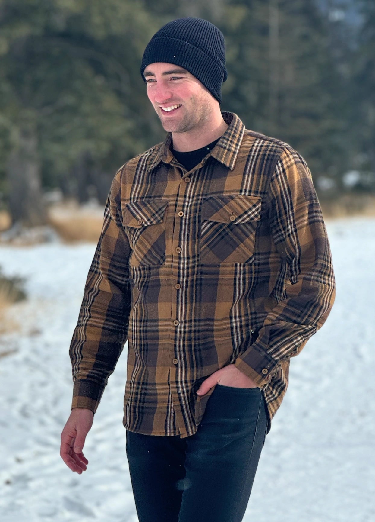 A man wearing a mocha brown flannel shirt with two flap breast pockets and a shirt tail hemline, standing outdoors.