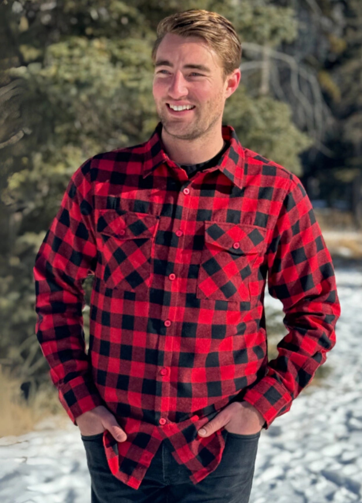 A man wearing a red and black buffalo check flannel shirt with two flap breast pockets and a button cuff, standing outdoors.