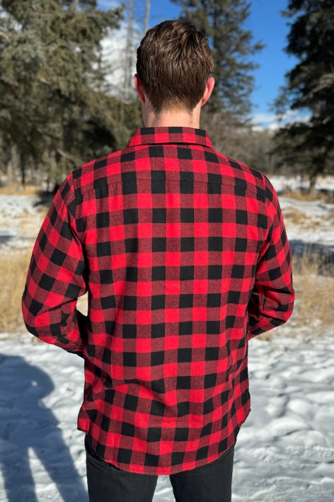 Back view of a man wearing a red and black buffalo check flannel shirt with two flap breast pockets and a button cuff, standing outdoors.