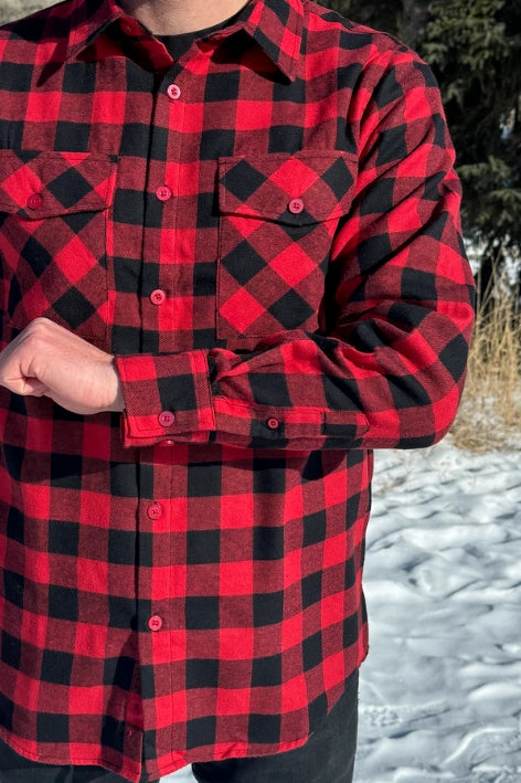 Close up of man wearing a red and black buffalo check flannel shirt with two flap breast pockets and a button cuff, standing outdoors.