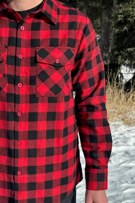 Close up of a man wearing a red and black buffalo check flannel shirt with two flap breast pockets and a button cuff, standing outdoors.