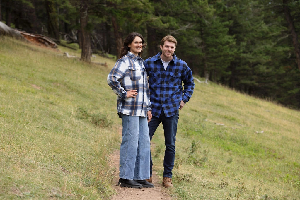 A man wearing a royal blue and black buffalo check padded flannel camping outdoor jacket with jeans.