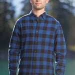 Man standing outdoors wearing long-sleeved marine blue and black buffalo check flannel shirt.