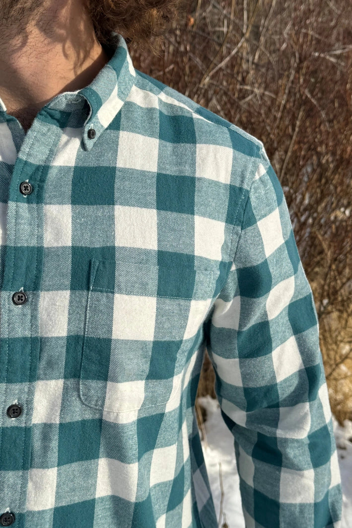 Close up of a man standing outdoors wearing a teal buffalo check flannel shirt with long sleeves, button-up collar, and a single breast pocket.