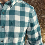 Close up of a man standing outdoors wearing a teal buffalo check flannel shirt with long sleeves, button-up collar, and a single breast pocket.