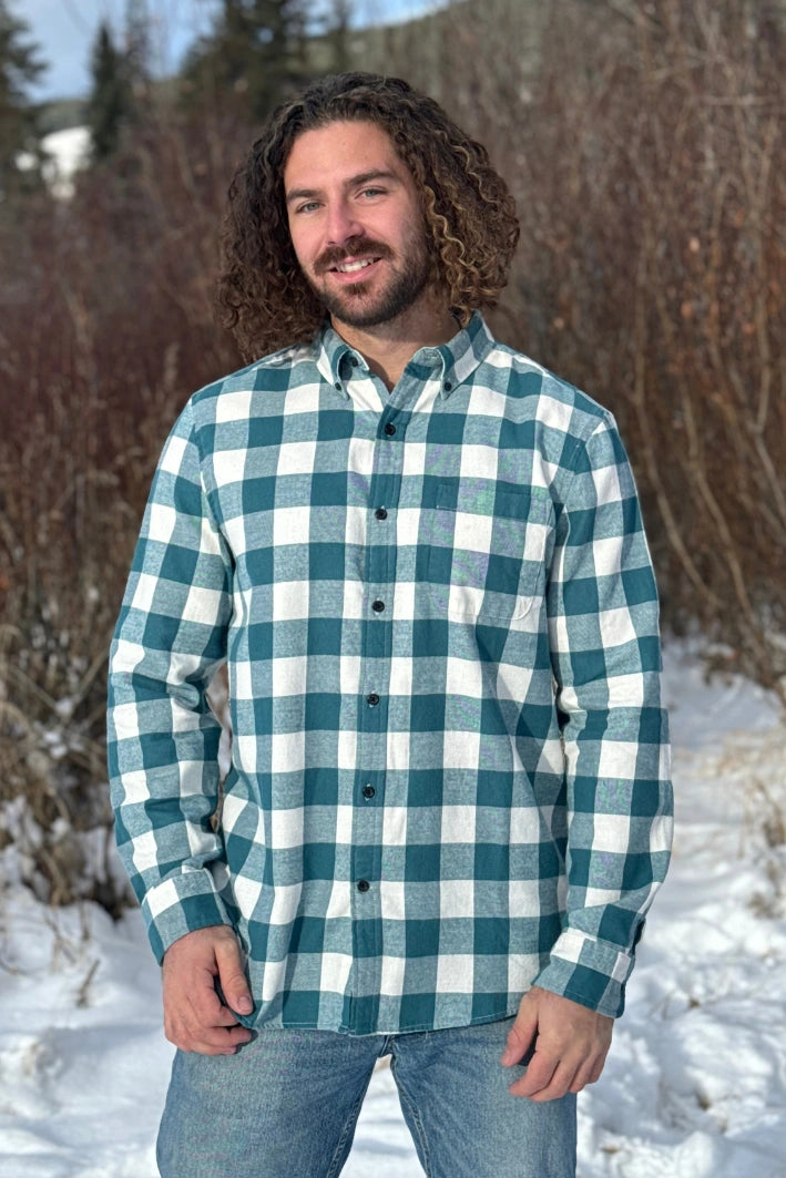 A man standing outdoors wearing a teal buffalo check flannel shirt with long sleeves, button-up collar, and a single breast pocket.