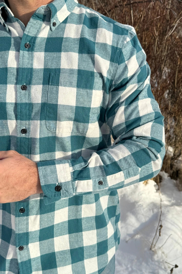 Close up of a man standing outdoors wearing a teal buffalo check flannel shirt with long sleeves, button-up collar, and a single breast pocket.