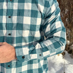 Close up of a man standing outdoors wearing a teal buffalo check flannel shirt with long sleeves, button-up collar, and a single breast pocket.