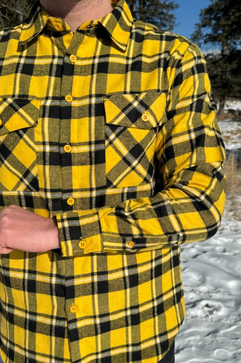 A man wearing a long-sleeved yellow and black flannel plaid shirt with two flap breast pockets and a button cuff.