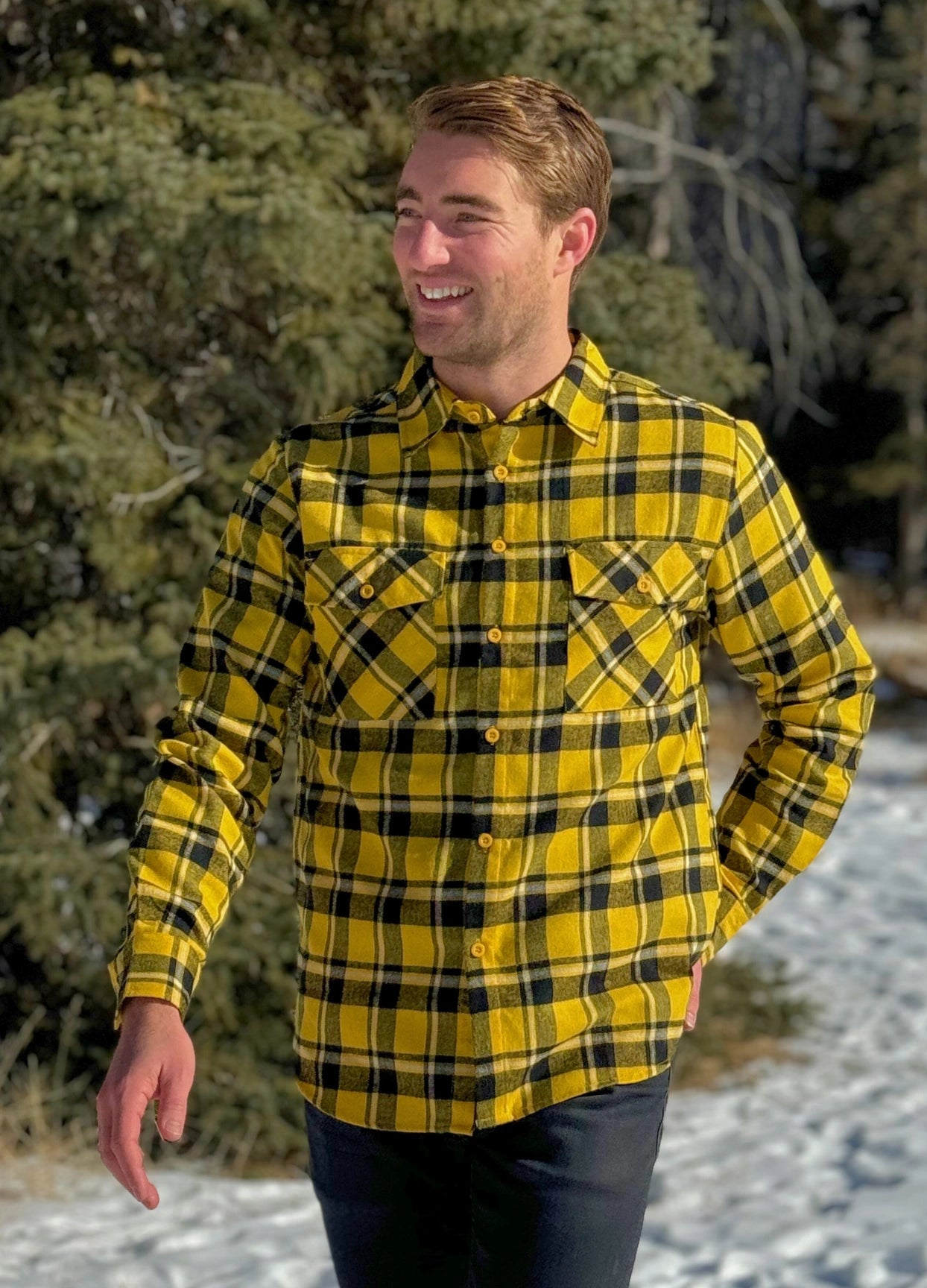 A man wearing a long-sleeved yellow and black flannel plaid shirt with two flap breast pockets and a button cuff.