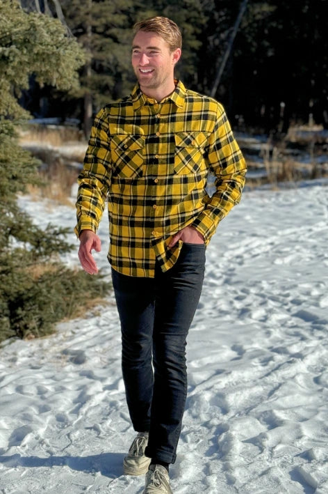 A man wearing a long-sleeved yellow and black flannel plaid shirt with two flap breast pockets and a button cuff.