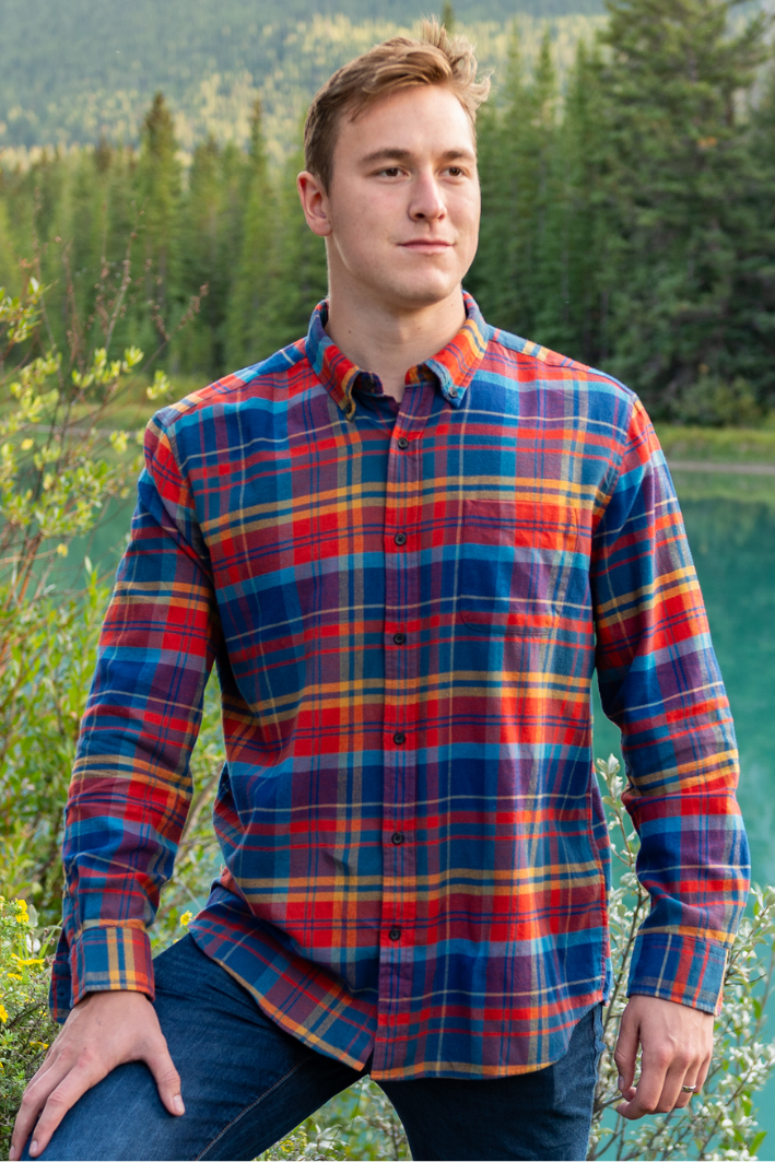 A man standing outdoors wearing a long-sleeved orange, red, and blue plaid flannel shirt with a collar.