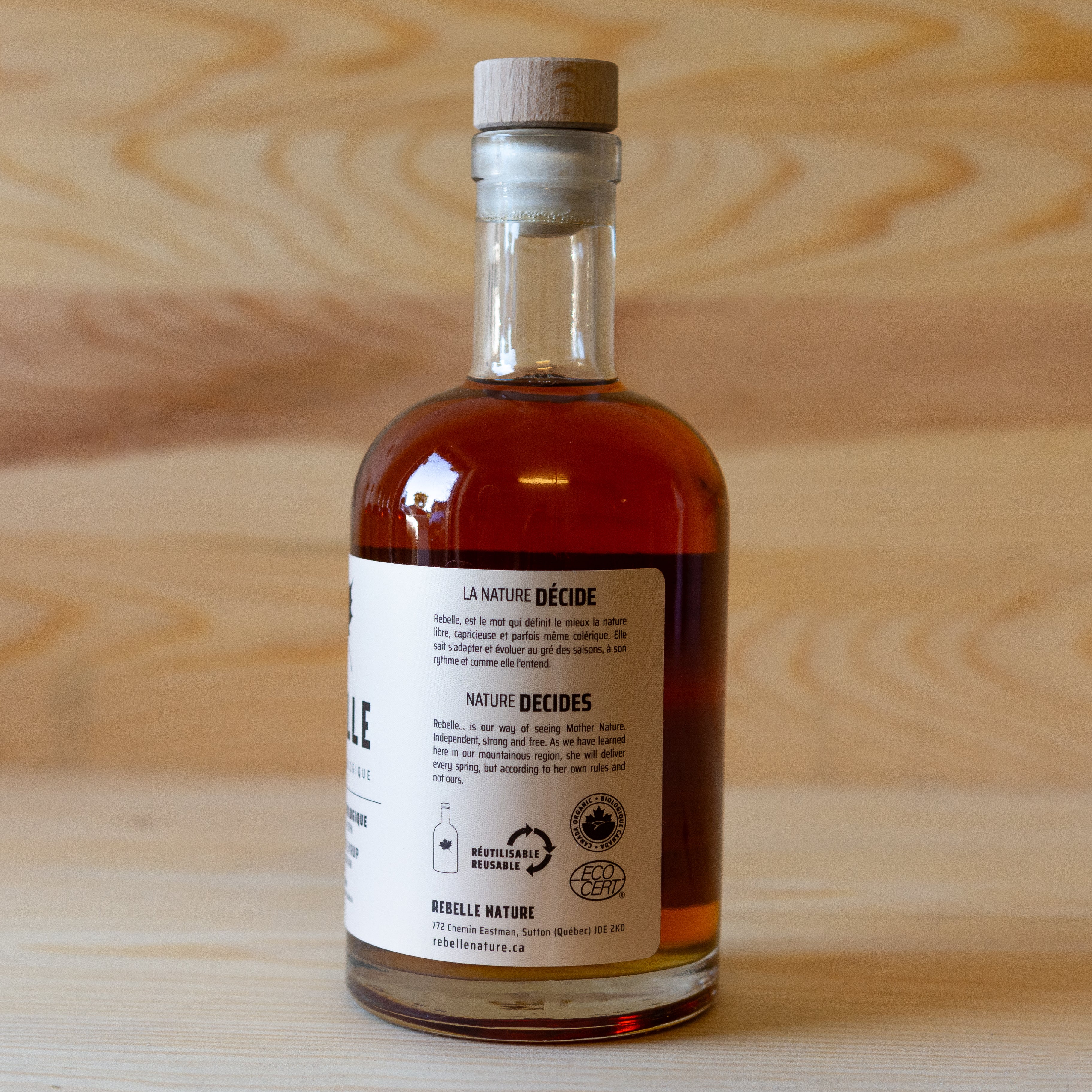 Back label of a bottle of Rebelle brand maple syrup with a wooden cap, placed on a wooden surface.