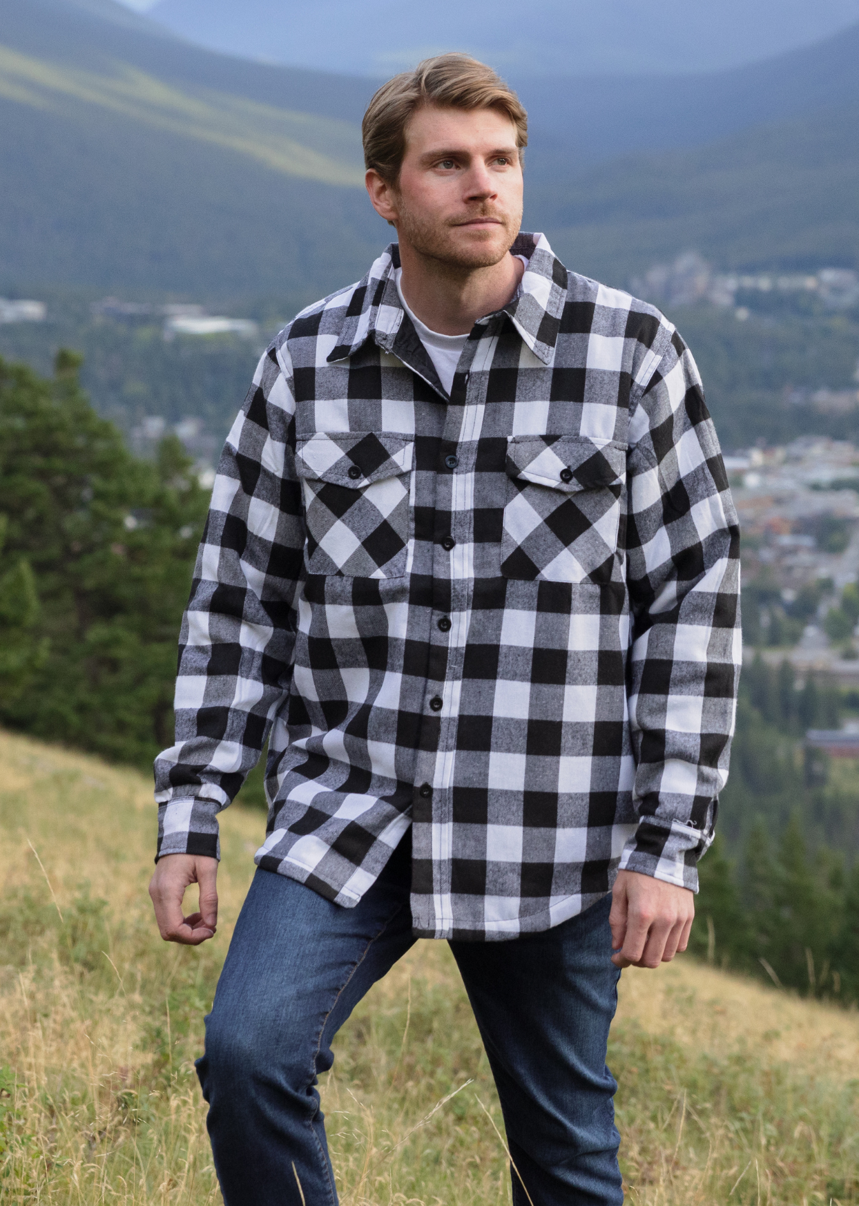 A man wearing a long-sleeved black and white checkered flannel padded jacket with a collar, button cuffs, and a shirttail hemline, standing outdoors.