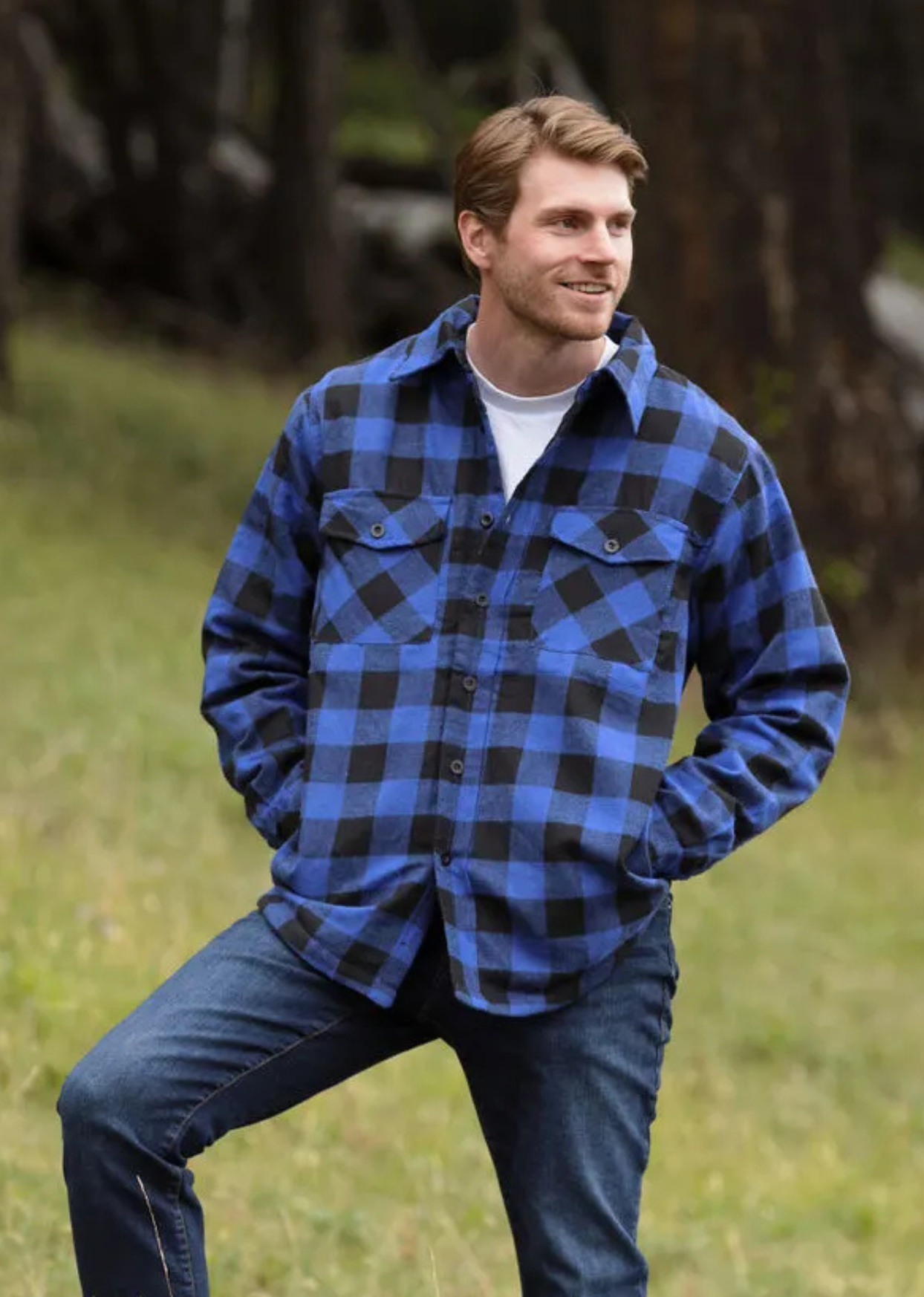 A man wearing a royal blue and black buffalo check padded flannel camping outdoor jacket with jeans.