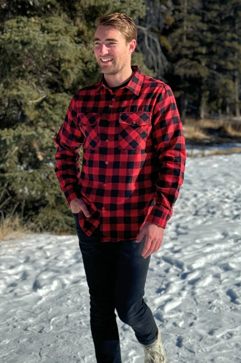 A man wearing a red and black buffalo check flannel shirt with two flap breast pockets and a button cuff, standing outdoors.