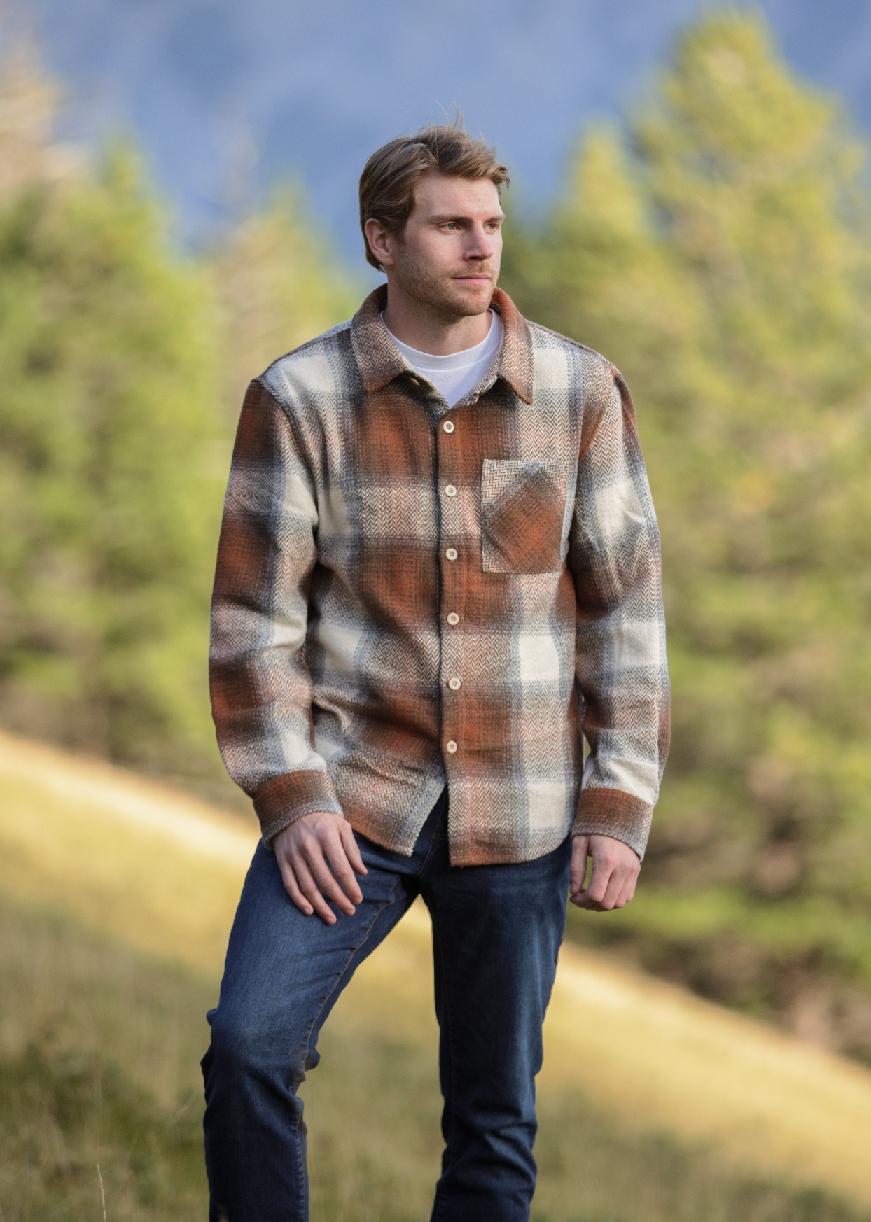 A person standing outdoors wearing a plaid flannel shacket with a herringbone weave in a blend of brown and blue colors.
