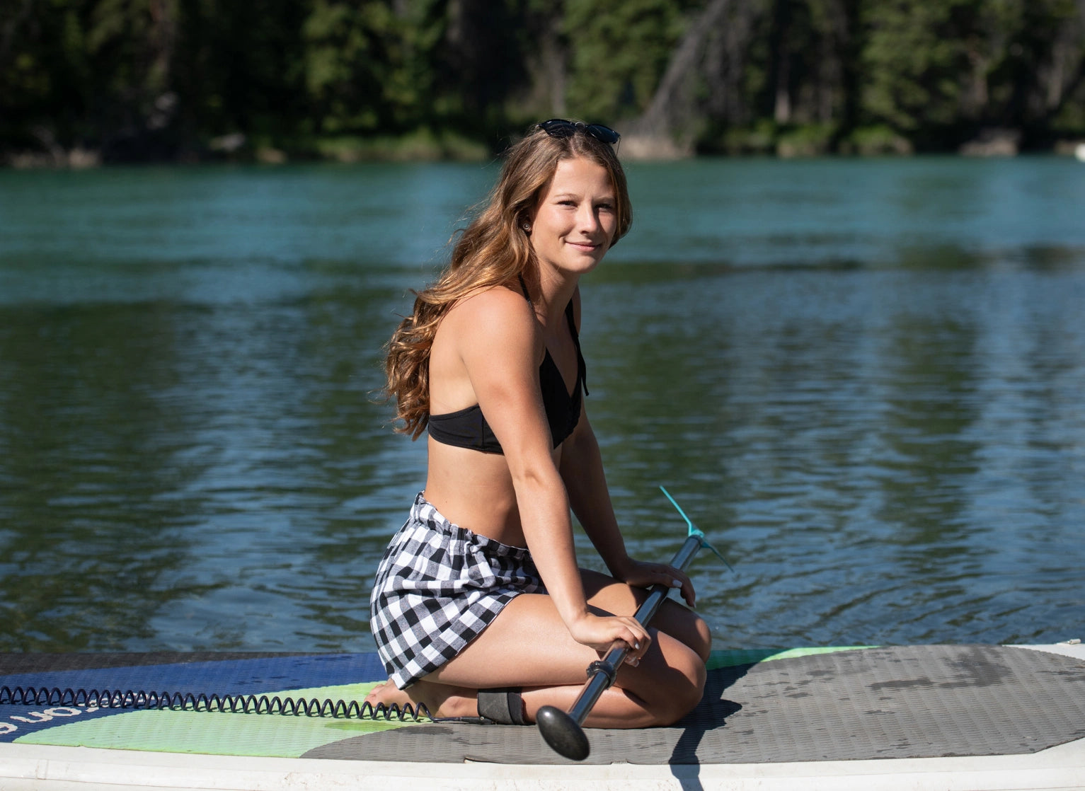 A girl paddle boarding wearing black and white buffalo check shorts